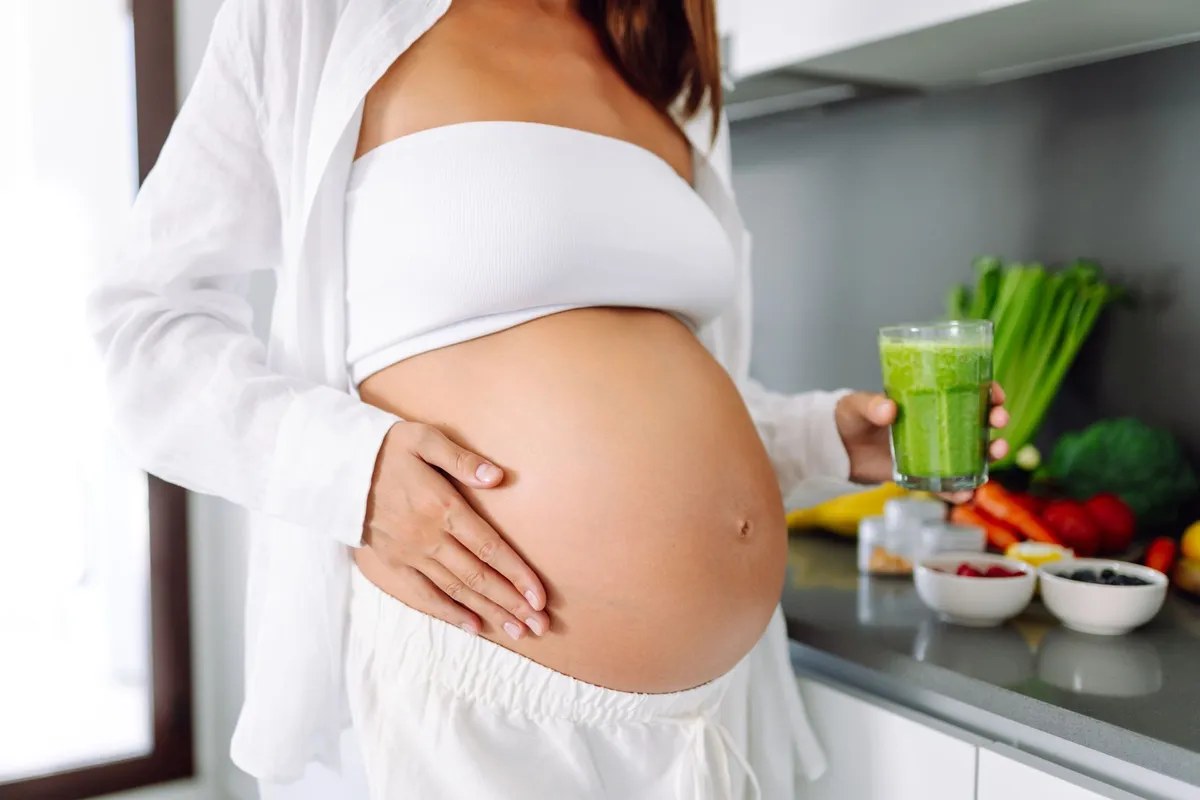 Gestante com um suco verde na cozinha